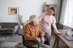 Two older adults using walkers walk side by side down a wide, sunlit hallway with supportive handrails.
